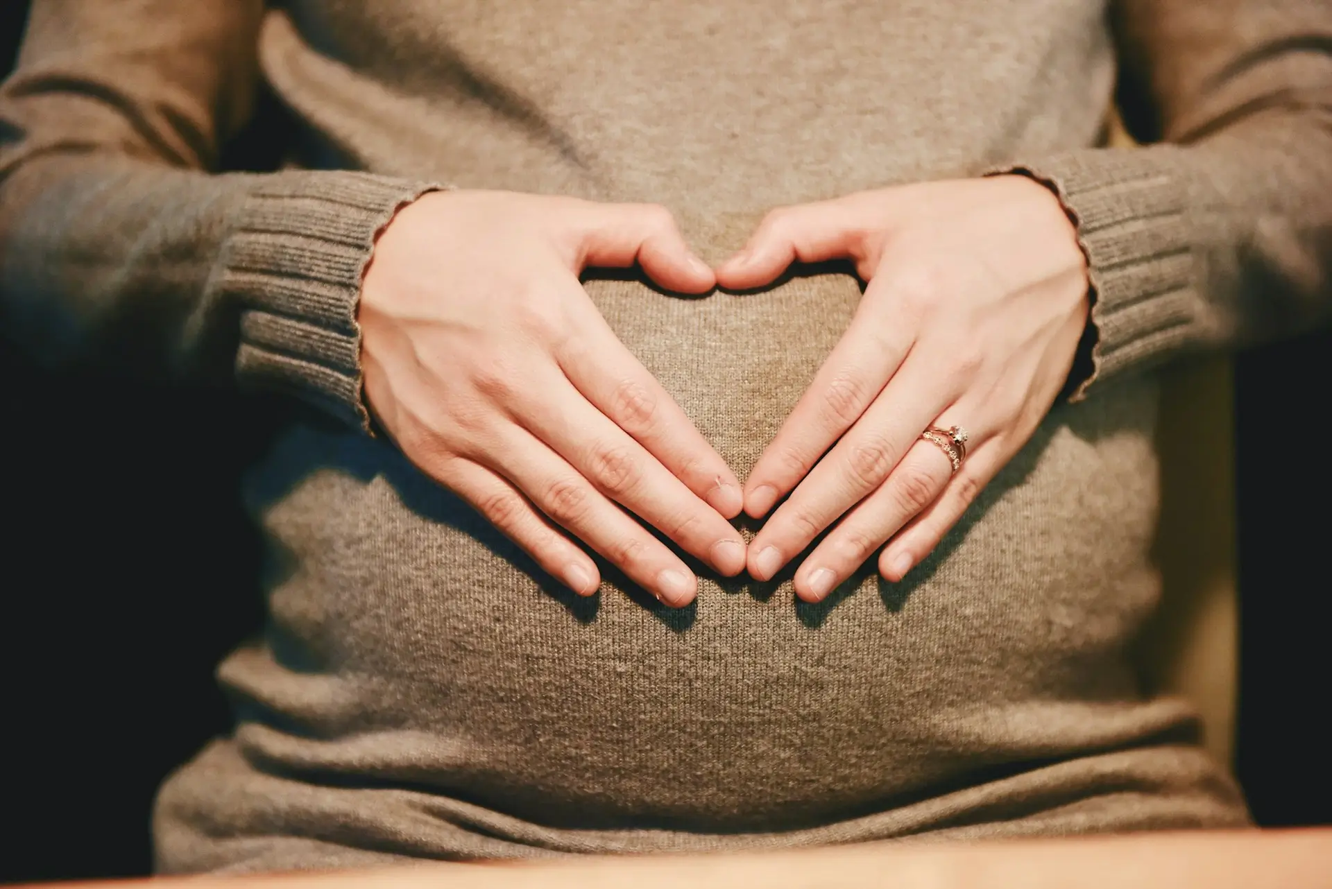 Hands forming heart over pregnant belly - our commitment to care